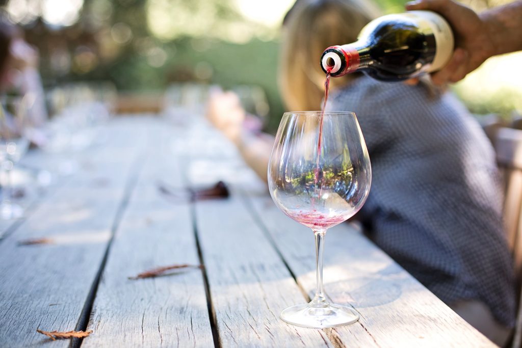 Mano che versa vino rosso italiano ad una tavolata di campagna sul lago di Garda